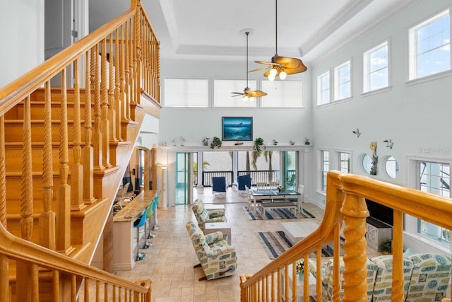 stairway featuring a tray ceiling, a healthy amount of sunlight, ornamental molding, and a ceiling fan