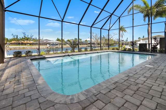 pool featuring glass enclosure, a patio, and a water view