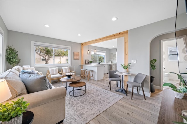 living area featuring arched walkways, baseboards, light wood-style flooring, and recessed lighting