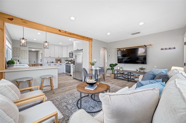 living room featuring light wood-type flooring, arched walkways, visible vents, and recessed lighting