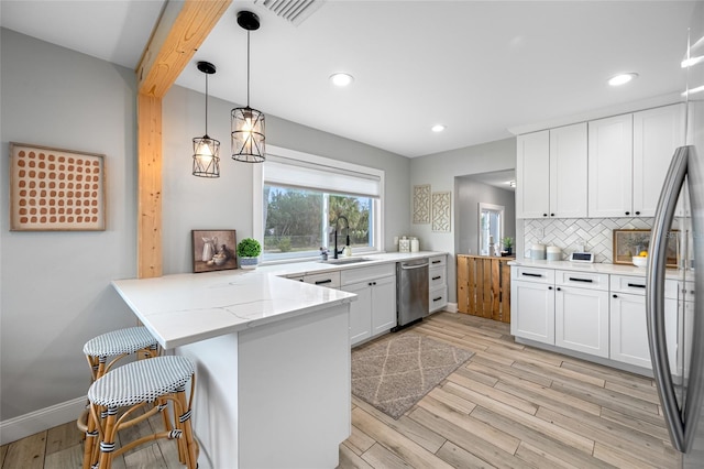 kitchen with stainless steel appliances, a peninsula, a sink, backsplash, and light wood finished floors