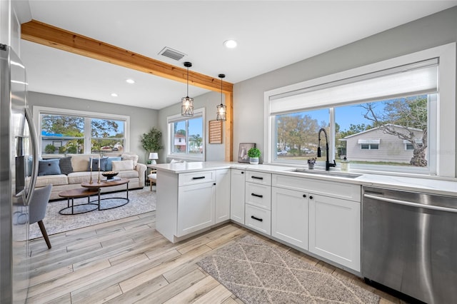 kitchen with visible vents, appliances with stainless steel finishes, open floor plan, a sink, and a peninsula