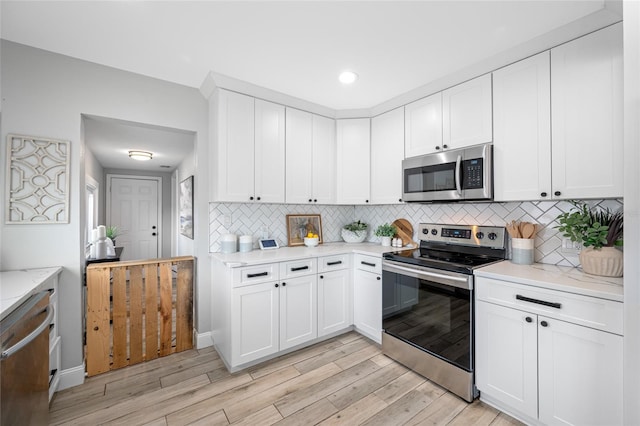 kitchen with light wood finished floors, white cabinets, decorative backsplash, light stone countertops, and stainless steel appliances