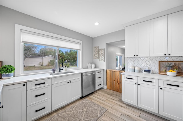 kitchen with backsplash, light wood-style floors, white cabinets, a sink, and dishwasher