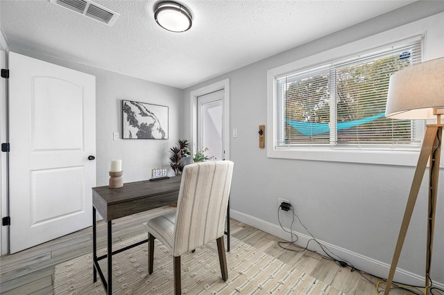 office space with visible vents, a textured ceiling, light wood-style flooring, and baseboards