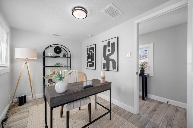 office with a healthy amount of sunlight, visible vents, baseboards, and light wood finished floors