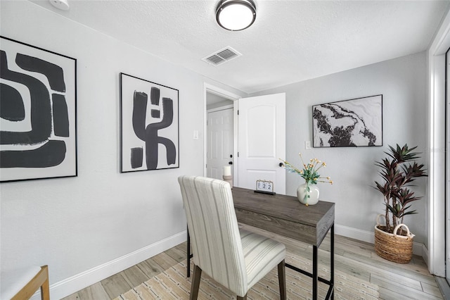 office with light wood-type flooring, visible vents, a textured ceiling, and baseboards