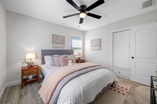 bedroom featuring light wood finished floors, visible vents, baseboards, ceiling fan, and a textured ceiling