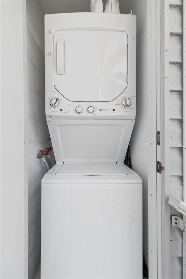 clothes washing area with stacked washer / drying machine, laundry area, and a textured wall