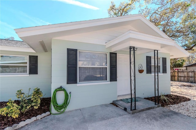 doorway to property featuring roof with shingles and fence