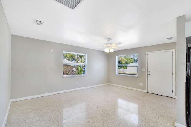 spare room featuring speckled floor, a ceiling fan, visible vents, and baseboards