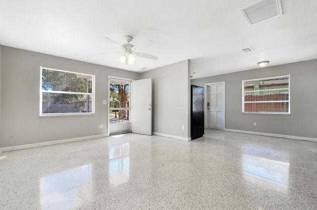 spare room with a ceiling fan, visible vents, baseboards, and speckled floor