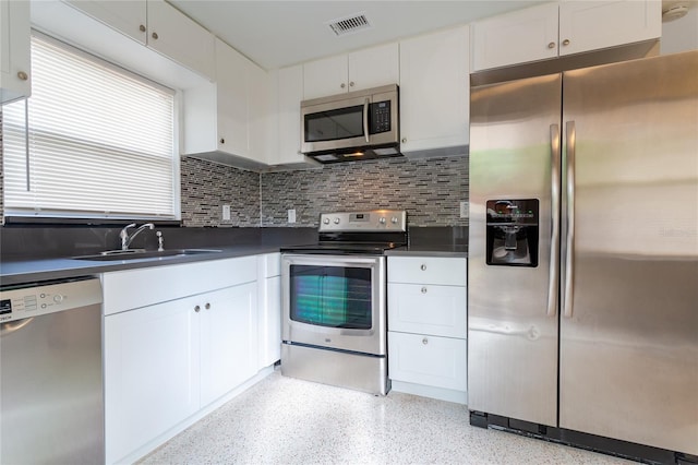 kitchen featuring light speckled floor, stainless steel appliances, a sink, white cabinetry, and dark countertops