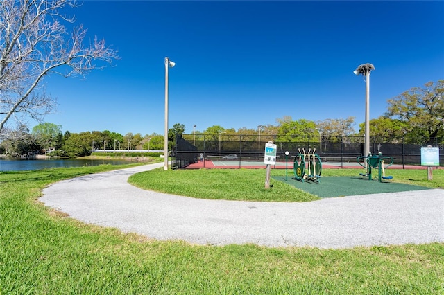 view of property's community featuring a yard, a water view, a tennis court, and fence