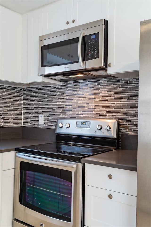 kitchen with stainless steel appliances, dark countertops, white cabinets, and tasteful backsplash