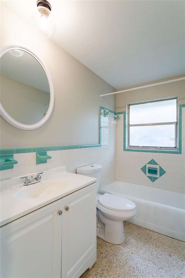 full bath featuring toilet, speckled floor, vanity, tile walls, and wainscoting