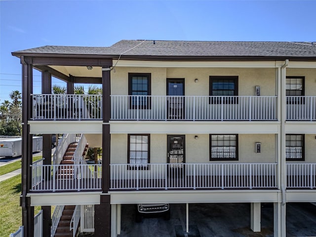 view of front of house with roof with shingles, stairs, and stucco siding