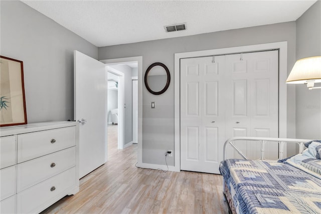 bedroom featuring a textured ceiling, visible vents, baseboards, a closet, and light wood-type flooring