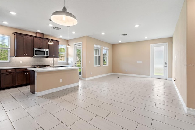 kitchen with a kitchen island with sink, dark brown cabinetry, light countertops, tasteful backsplash, and stainless steel microwave