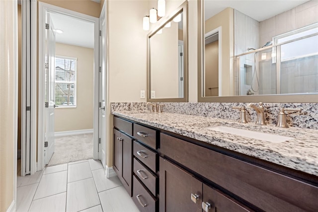 full bath featuring a sink, double vanity, a shower stall, and baseboards