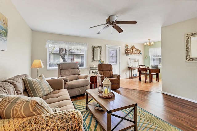 living room featuring ceiling fan with notable chandelier, baseboards, and wood finished floors