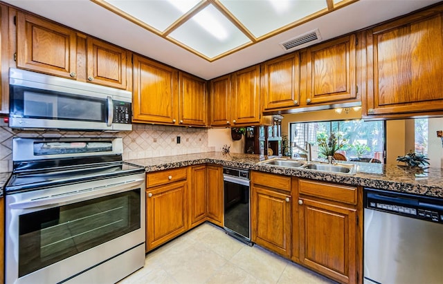 kitchen with dark countertops, visible vents, appliances with stainless steel finishes, brown cabinetry, and a sink