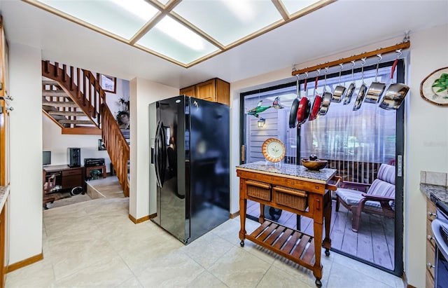 kitchen with stone counters, baseboards, brown cabinets, and black fridge