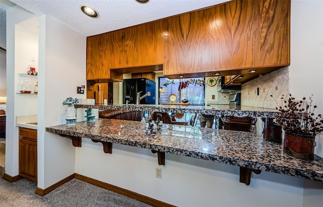 kitchen featuring brown cabinets, decorative backsplash, freestanding refrigerator, a textured ceiling, and baseboards