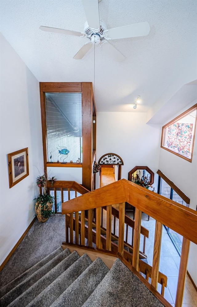 stairway with a textured ceiling, carpet floors, and baseboards