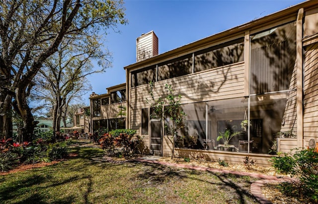 back of property featuring a balcony, a sunroom, a chimney, and a yard