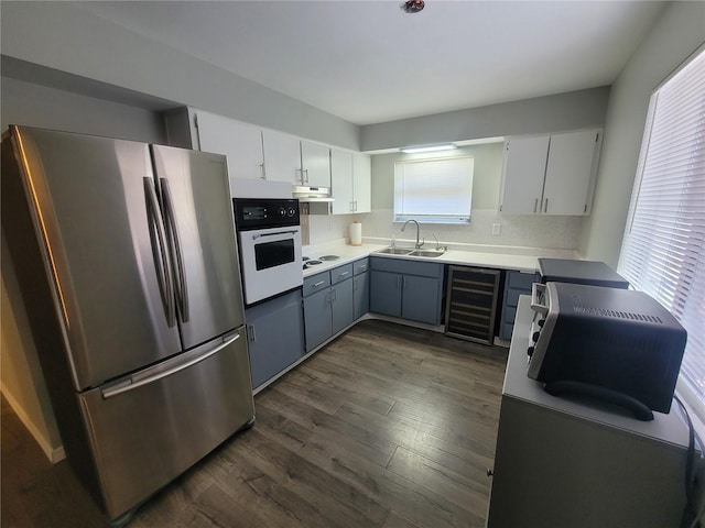 kitchen with under cabinet range hood, beverage cooler, white appliances, a sink, and dark wood-style floors