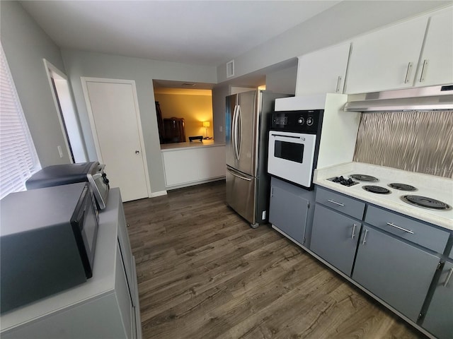 kitchen with under cabinet range hood, white appliances, dark wood-style flooring, visible vents, and light countertops