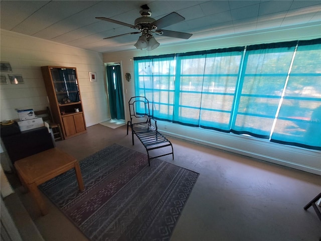 living area with ceiling fan, concrete floors, and concrete block wall