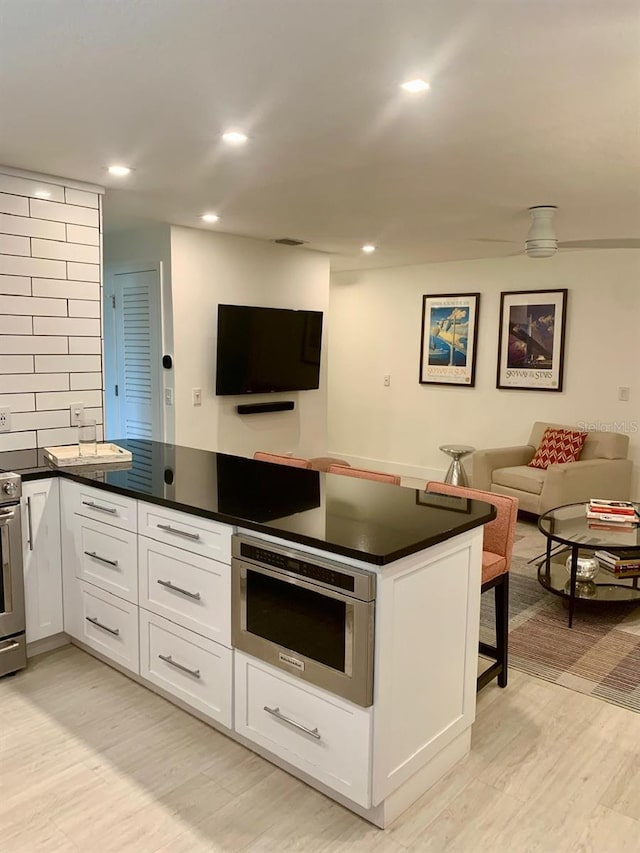 kitchen with white cabinets, light wood finished floors, dark countertops, and open floor plan