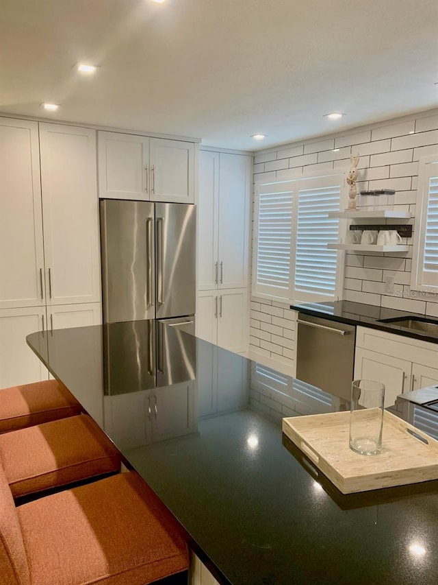 kitchen featuring stainless steel appliances, white cabinets, a sink, and backsplash