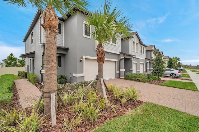 view of front facade featuring a garage, decorative driveway, fence, and stucco siding