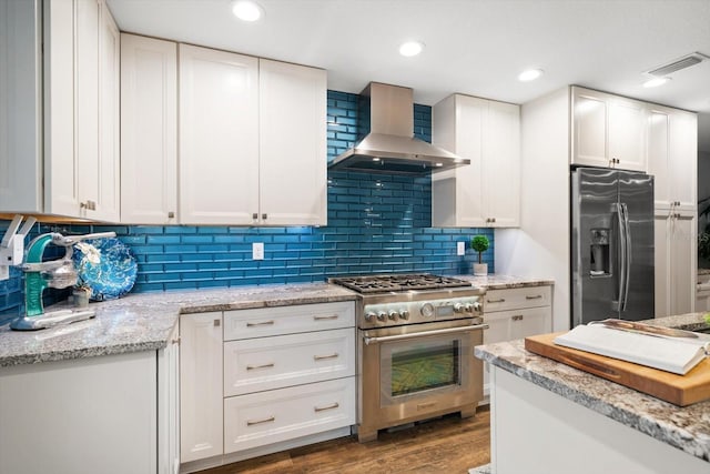 kitchen with stainless steel appliances, backsplash, white cabinetry, wood finished floors, and wall chimney exhaust hood