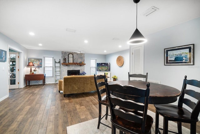 dining room featuring visible vents, baseboards, hardwood / wood-style flooring, a stone fireplace, and recessed lighting