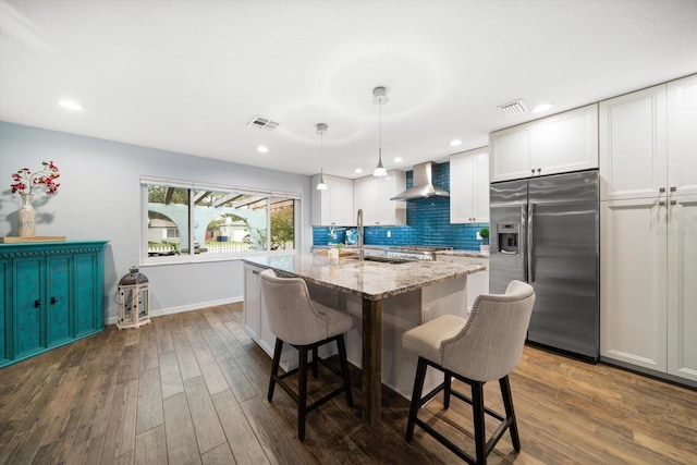 kitchen with decorative backsplash, wall chimney exhaust hood, dark wood-type flooring, stainless steel refrigerator with ice dispenser, and a sink