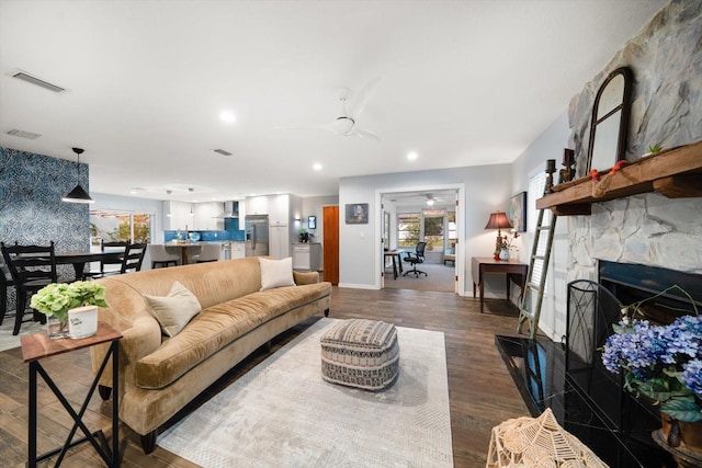 living area featuring dark wood-style floors, visible vents, a wealth of natural light, and a stone fireplace