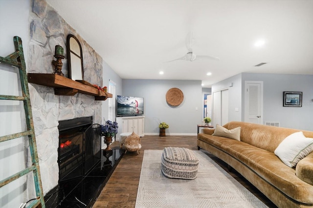 living room with visible vents, dark wood finished floors, a stone fireplace, and baseboards