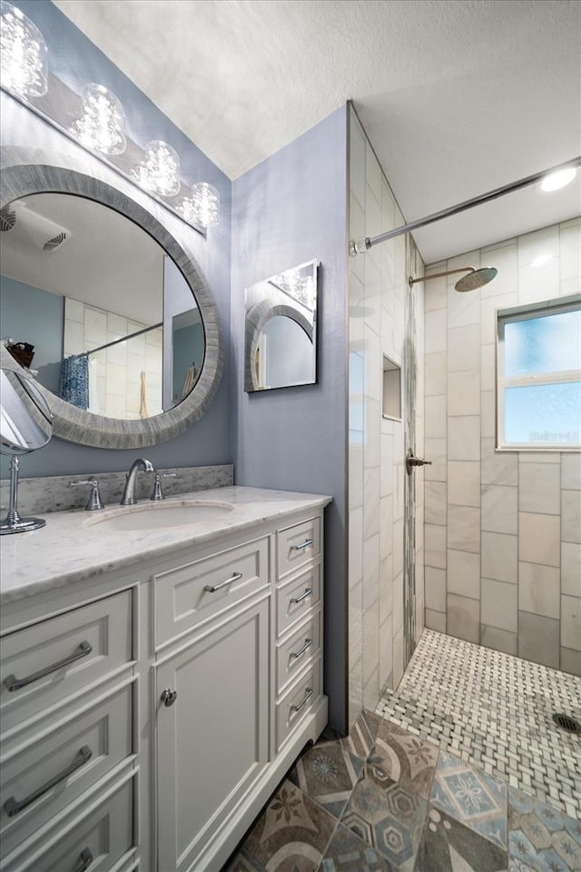 full bathroom with a textured ceiling, a tile shower, and vanity