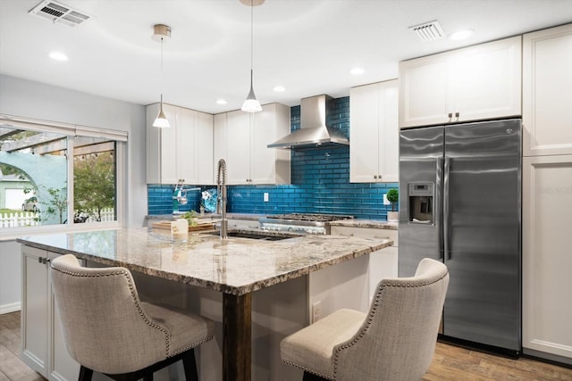 kitchen featuring tasteful backsplash, visible vents, light wood-style floors, wall chimney range hood, and stainless steel fridge with ice dispenser