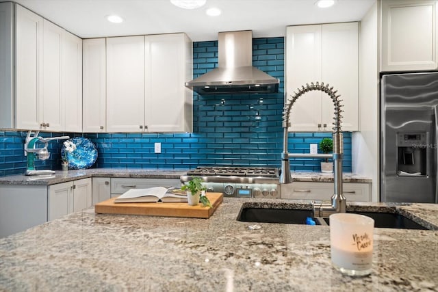 kitchen with wall chimney range hood, stainless steel refrigerator with ice dispenser, decorative backsplash, and white cabinets