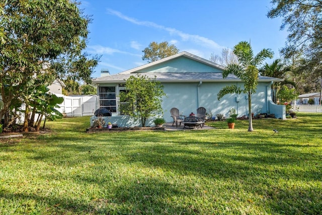 rear view of house featuring a yard, an outdoor fire pit, fence, and stucco siding