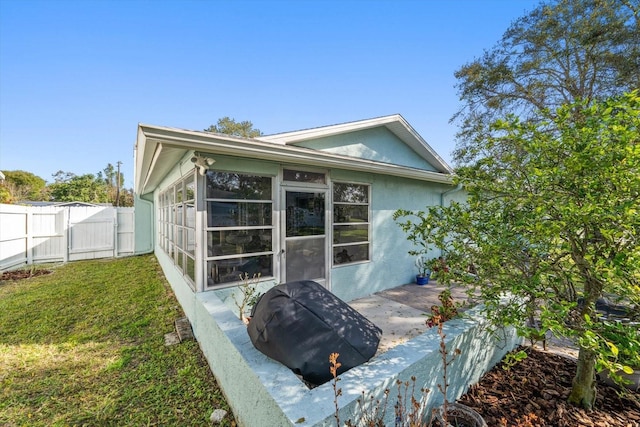 view of side of home featuring stucco siding, a lawn, a gate, a sunroom, and fence