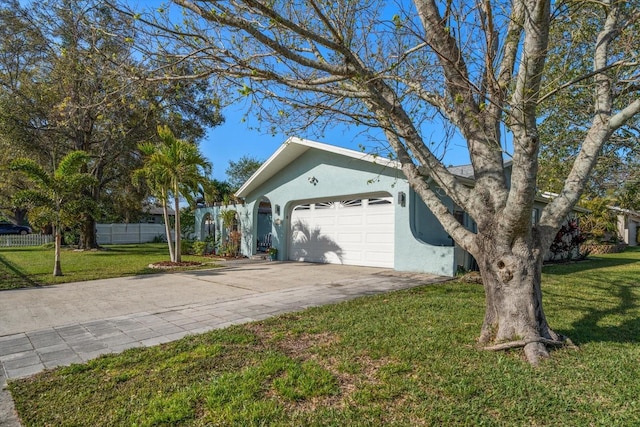 view of side of home with driveway, a lawn, an attached garage, fence, and stucco siding