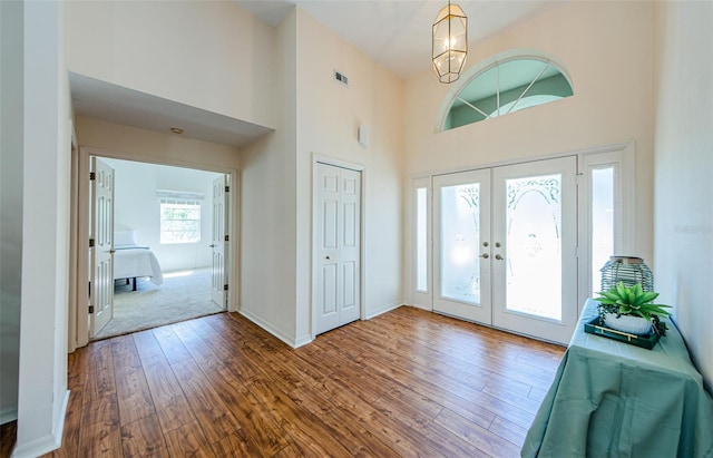 foyer entrance featuring visible vents, wood finished floors, french doors, a high ceiling, and baseboards