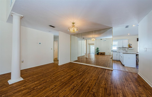 unfurnished living room with decorative columns, visible vents, wood-type flooring, and a chandelier