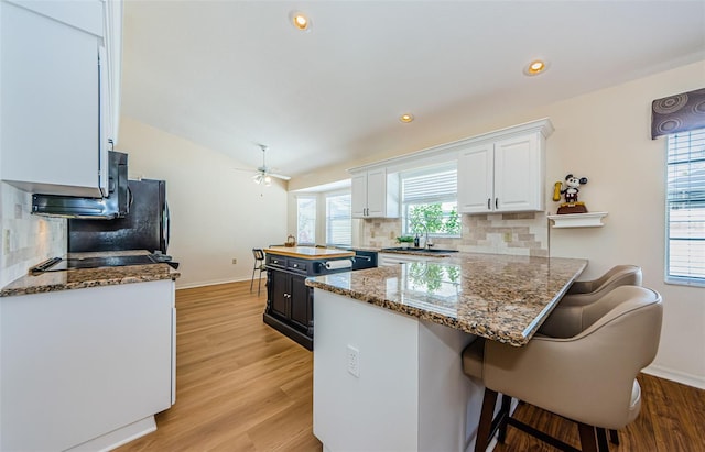 kitchen with a center island, vaulted ceiling, stone counters, white cabinetry, and a sink